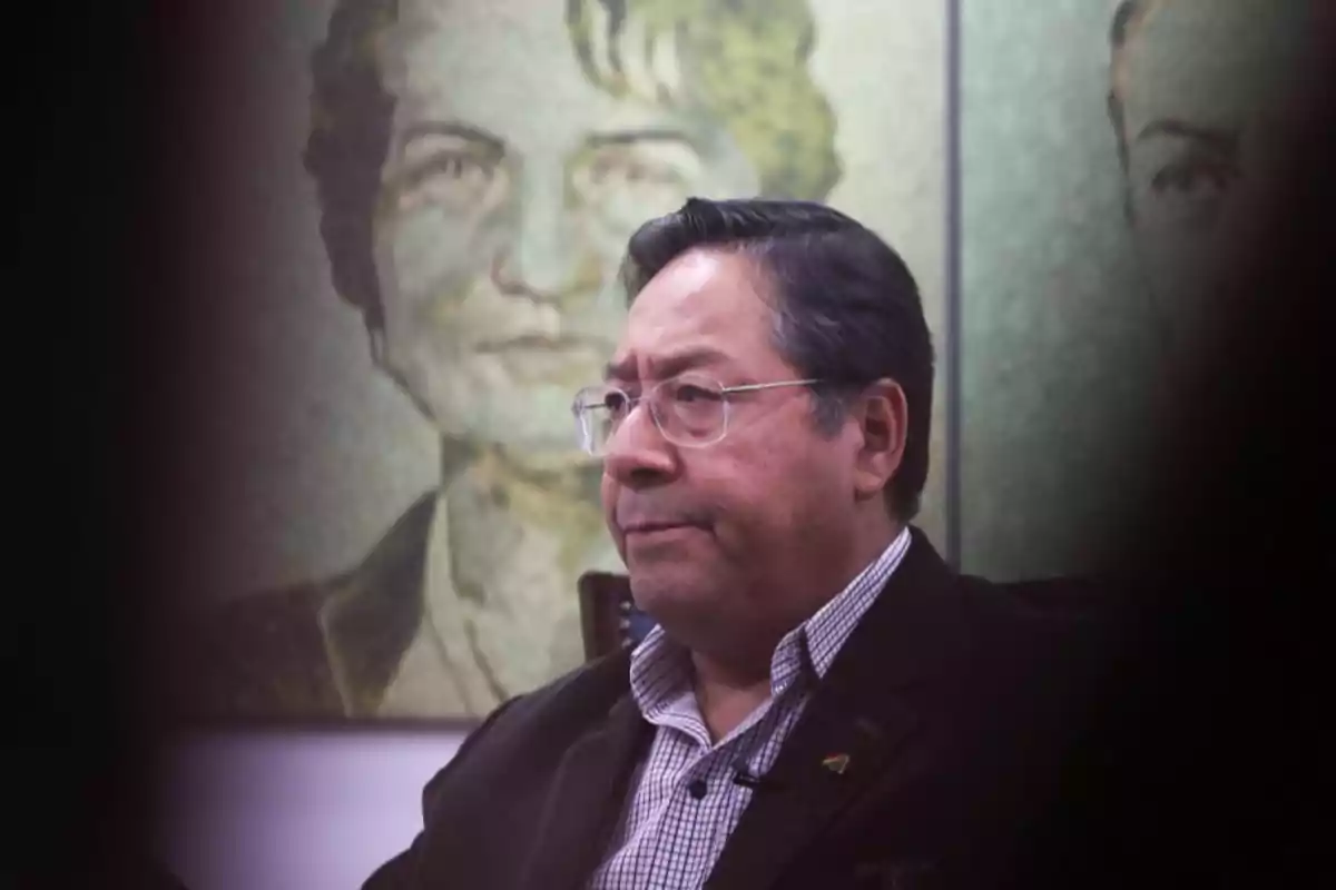 Hombre de cabello oscuro y gafas sentado frente a un cuadro con un retrato difuminado al fondo Hombre de cabello oscuro y gafas sentado frente a un cuadro con un retrato difuminado al fondo