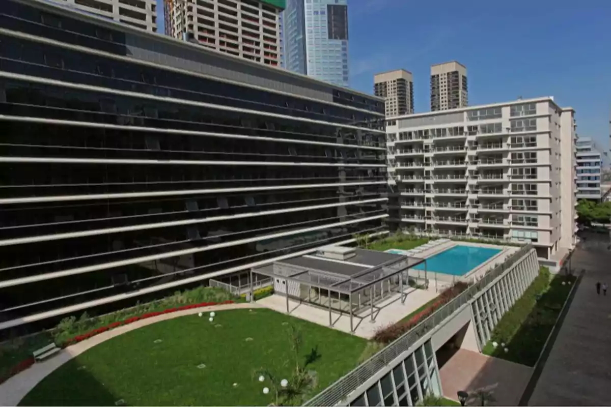 Vista de un complejo residencial moderno con áreas verdes, una piscina y edificios altos rodeando el espacio central Vista de un complejo residencial moderno con áreas verdes, una piscina y edificios altos rodeando el espacio central