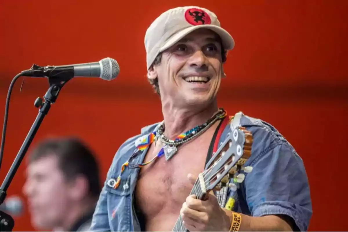 Smiling man with a beige cap and guitar playing in front of a microphone on a red background stage Smiling man with a beige cap and guitar playing in front of a microphone on a red background stage