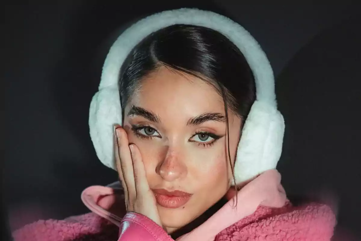Young woman with white earmuffs and a pink jacket looking at the camera with her hand on her cheek