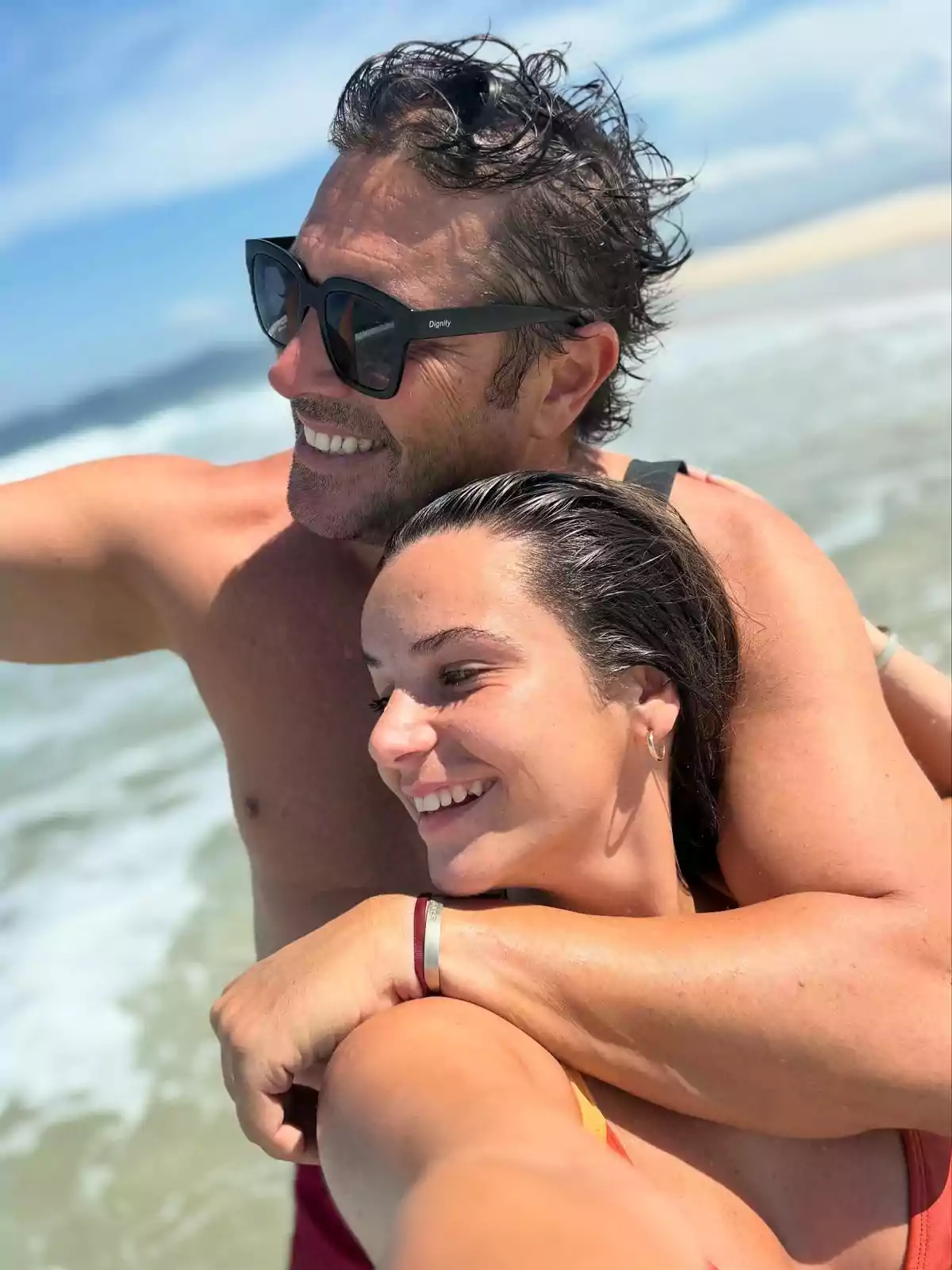 Pareja sonriente tomándose una selfie en la playa con el mar de fondo en un día soleado Pareja sonriente tomándose una selfie en la playa con el mar de fondo en un día soleado