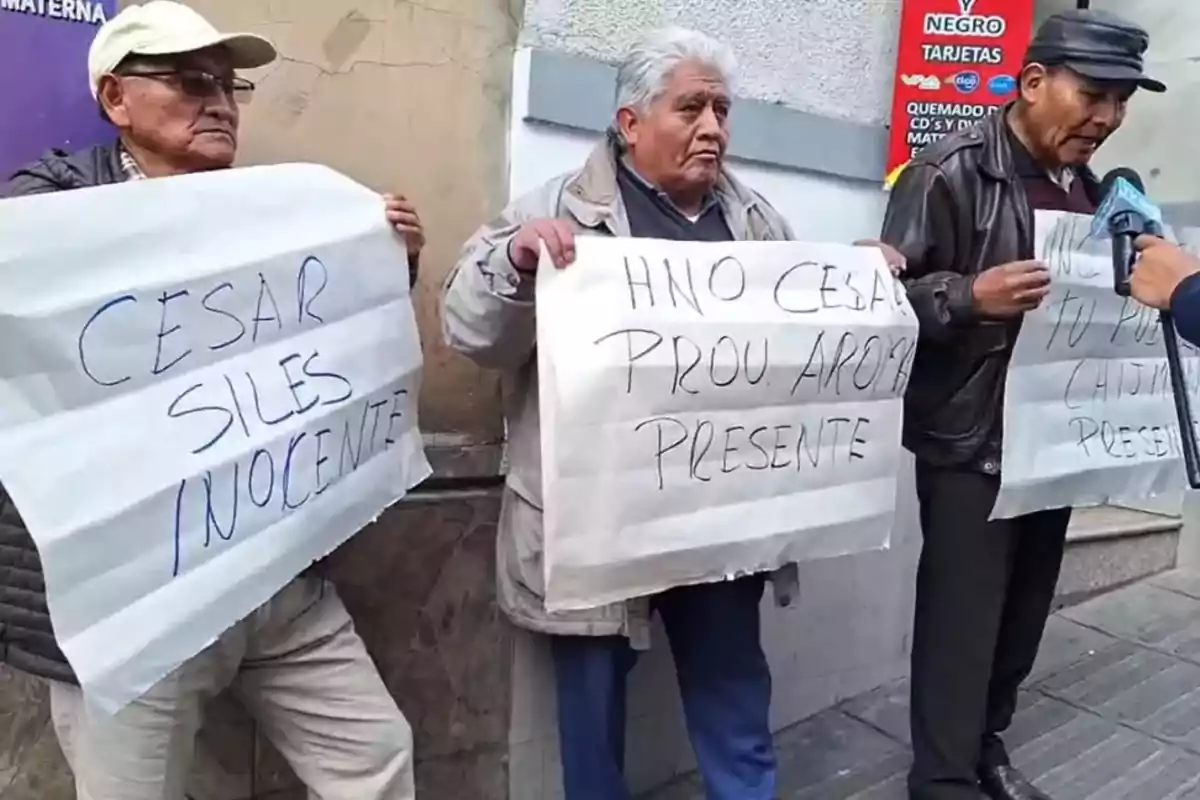 Three elderly men are standing on the street holding handmade signs expressing support for someone named César Siles and calling for justice. Three elderly men are standing on the street holding handmade signs expressing support for someone named César Siles and calling for justice.