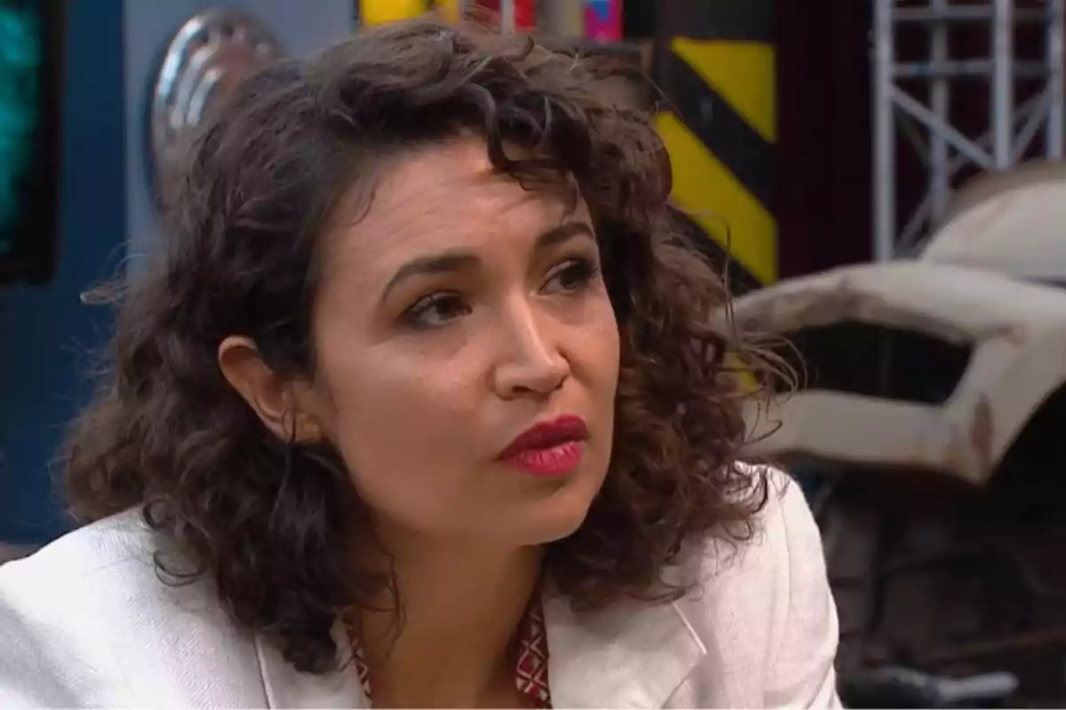 Mujer de cabello rizado y corto con chaqueta blanca mirando hacia un lado en un entorno industrial