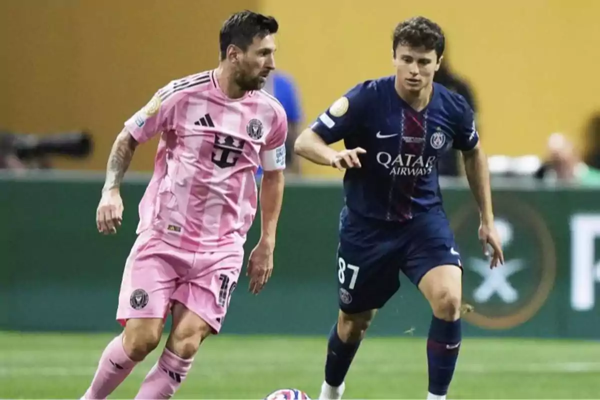Dos futbolistas disputan el balón durante un partido, uno con uniforme rosa y el otro con uniforme azul marino. Dos futbolistas disputan el balón durante un partido, uno con uniforme rosa y el otro con uniforme azul marino.