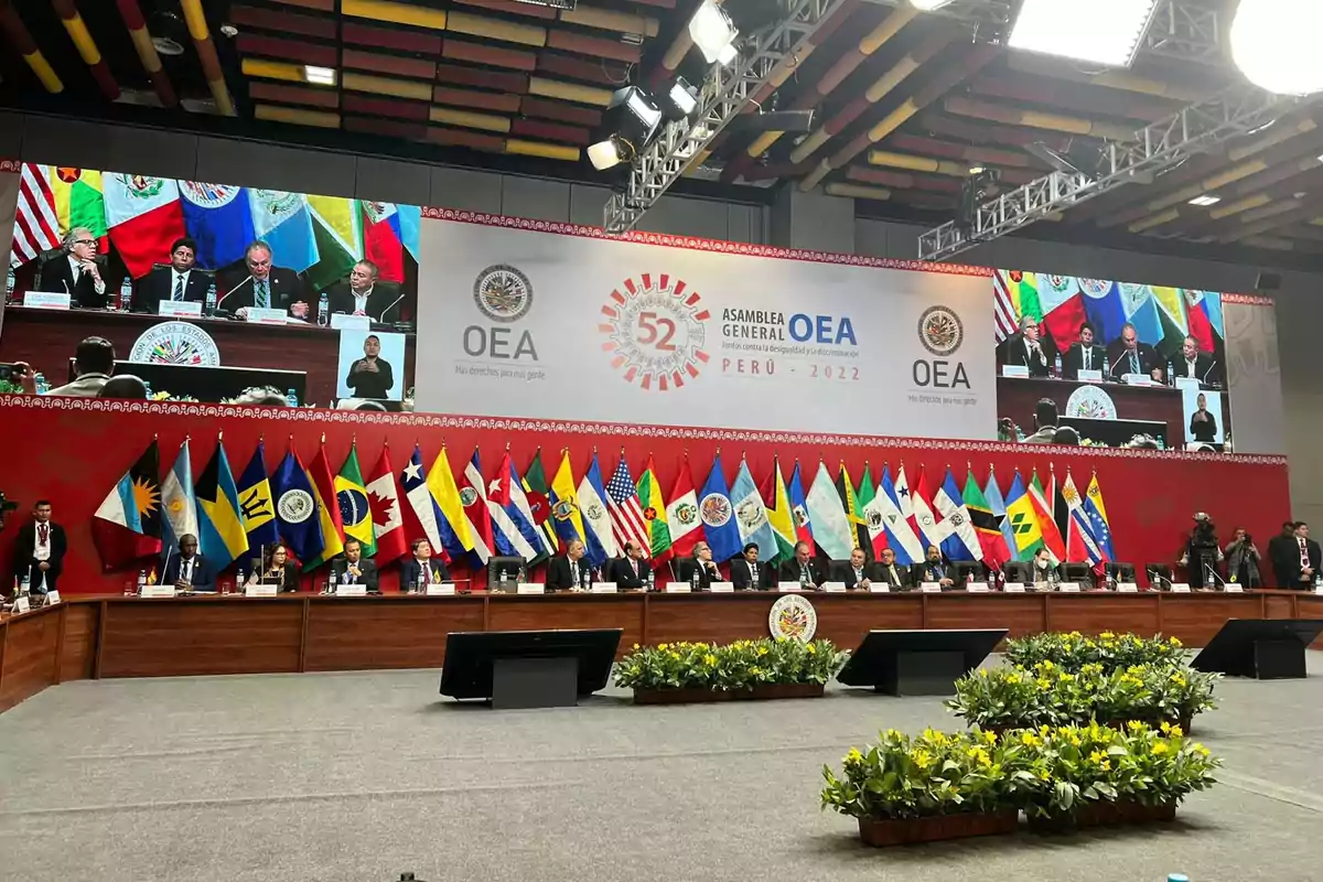 Reunión de representantes de países miembros de la OEA en una sala de conferencias decorada con banderas nacionales y un gran cartel que indica la 52 Asamblea General en Perú 2022 Reunión de representantes de países miembros de la OEA en una sala de conferencias decorada con banderas nacionales y un gran cartel que indica la 52 Asamblea General en Perú 2022