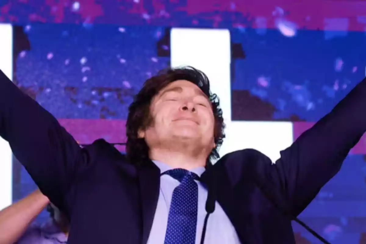 Hombre con traje y corbata levantando los brazos y sonriendo con los ojos cerrados frente a un fondo colorido