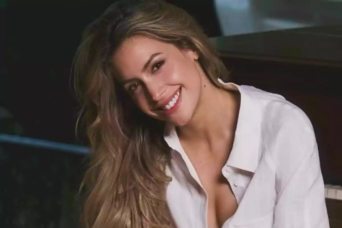 Mujer joven de cabello largo y ondulado sonríe mientras lleva puesta una camisa blanca