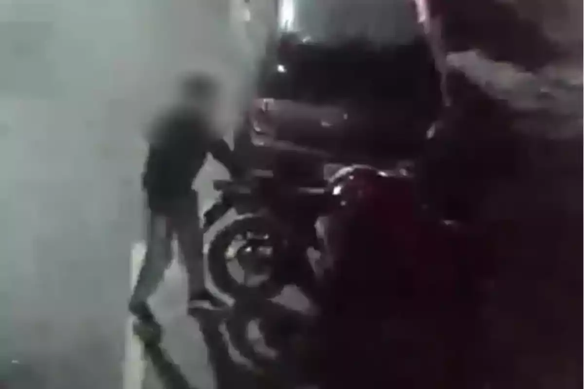 Person standing next to a motorcycle on a dark street with a parked car in the background Person standing next to a motorcycle on a dark street with a parked car in the background