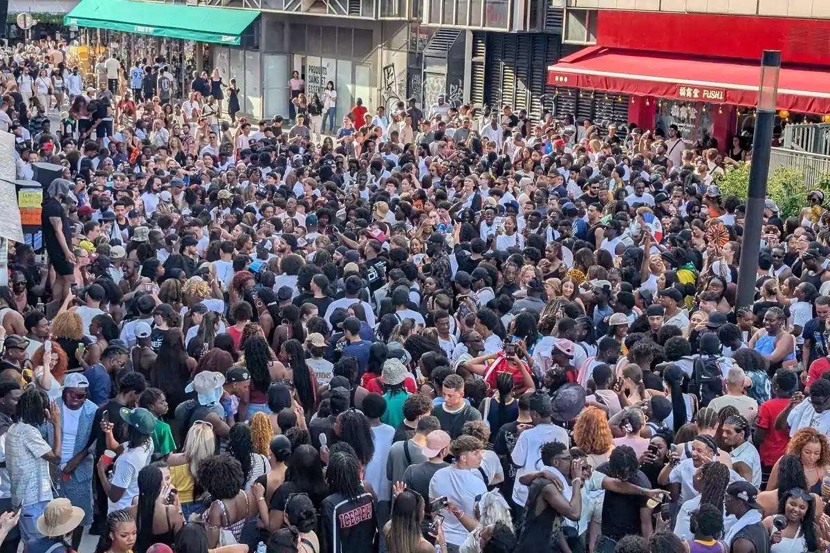 Una multitud de personas reunidas en una calle peatonal durante un evento al aire libre en un día soleado
