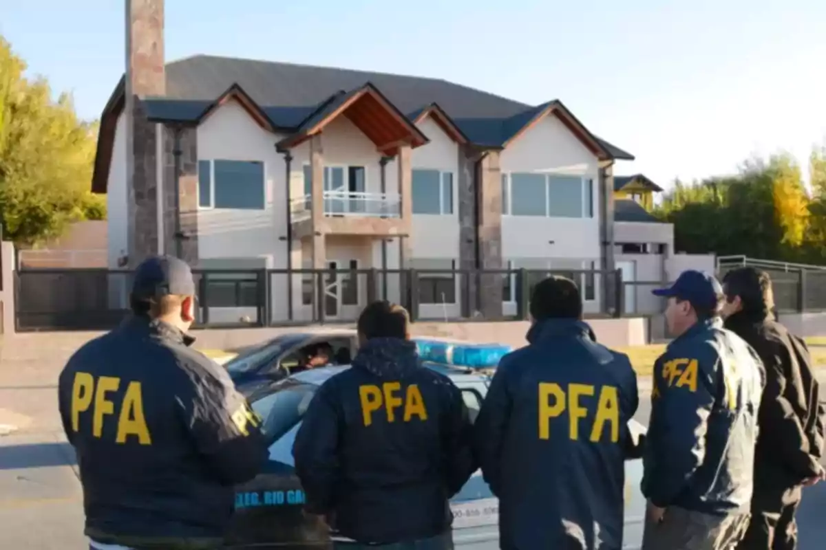 Five agents wearing PFA jackets are standing in front of a large, modern house while observing a police operation. Five agents wearing PFA jackets are standing in front of a large, modern house while observing a police operation.