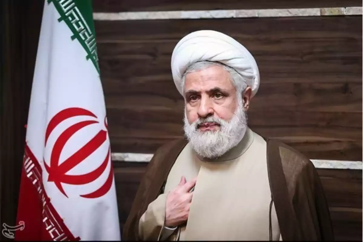 Man in traditional Islamic clothing and a white turban standing next to an Iranian flag against a wooden background Man in traditional Islamic clothing and a white turban standing next to an Iranian flag against a wooden background