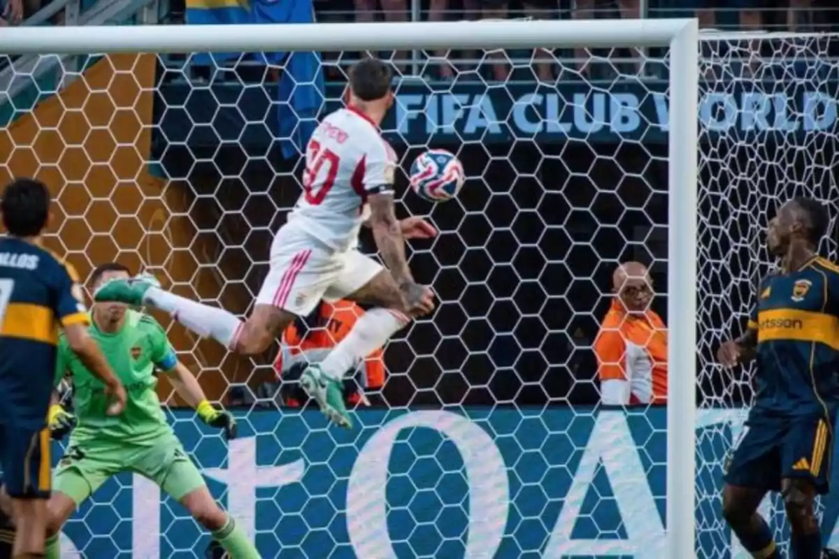 Jugador de fútbol con uniforme blanco y rojo remata de volea frente a la portería mientras el portero y defensores con uniforme azul y amarillo intentan evitar el gol durante un partido importante Jugador de fútbol con uniforme blanco y rojo remata de volea frente a la portería mientras el portero y defensores con uniforme azul y amarillo intentan evitar el gol durante un partido importante
