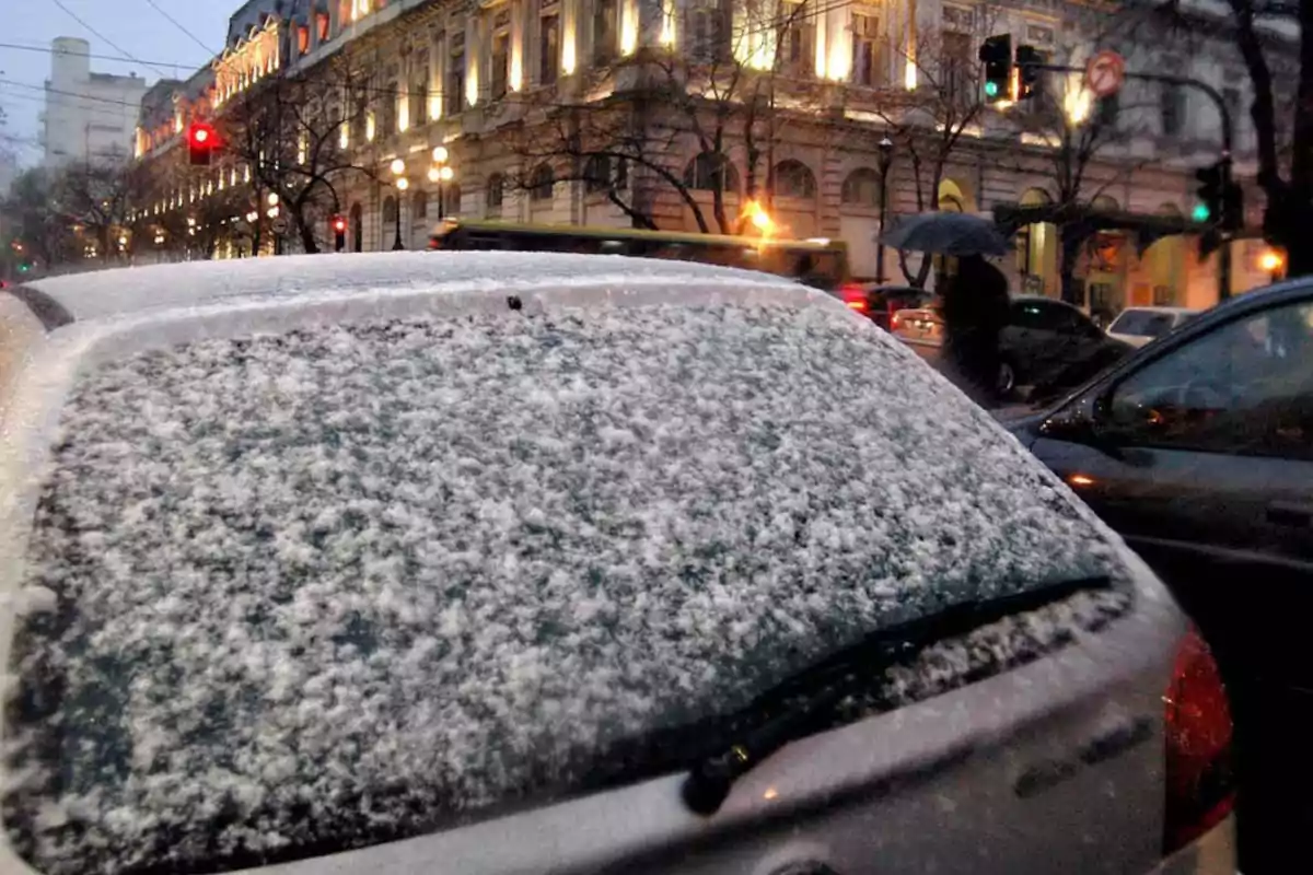 Un auto cubierto de nieve estacionado en una calle de ciudad con edificios iluminados y personas caminando bajo la lluvia Un auto cubierto de nieve estacionado en una calle de ciudad con edificios iluminados y personas caminando bajo la lluvia