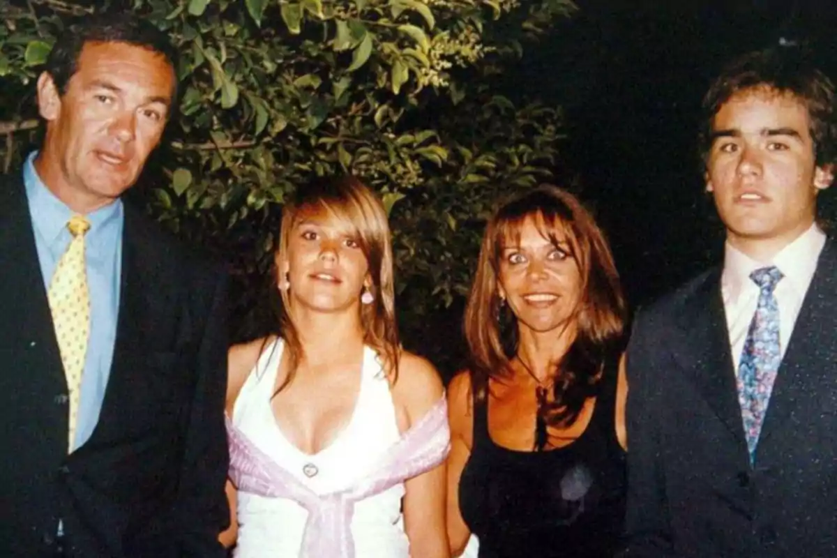Four people pose together outdoors, two men and two women, all dressed formally with trees in the background. Four people pose together outdoors, two men and two women, all dressed formally with trees in the background.