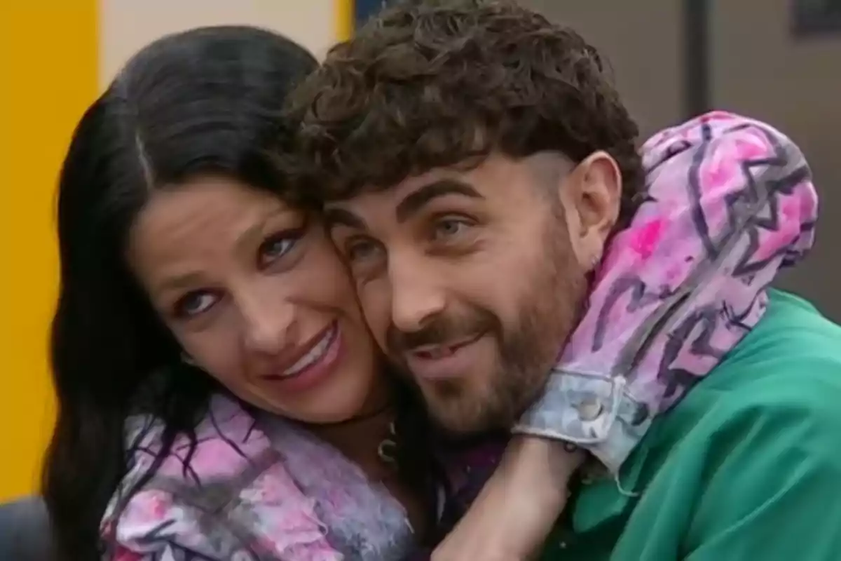 Two people hugging and smiling, a dark-haired woman and a curly-haired man with a beard, both looking happy and close. Two people hugging and smiling, a dark-haired woman and a curly-haired man with a beard, both looking happy and close.