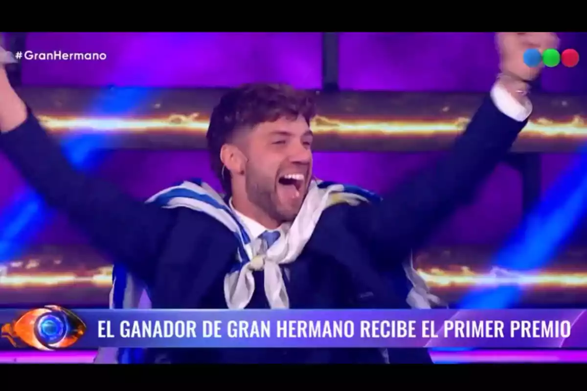 Un hombre joven celebra con los brazos en alto envuelto en una bandera mientras en la pantalla se lee el mensaje el ganador de Gran Hermano recibe el primer premio Un hombre joven celebra con los brazos en alto envuelto en una bandera mientras en la pantalla se lee el mensaje el ganador de Gran Hermano recibe el primer premio