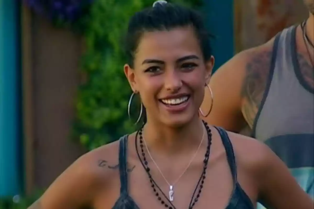 Young woman with dark hair tied back, smiling outdoors, wearing large earrings and necklaces Young woman with dark hair tied back, smiling outdoors, wearing large earrings and necklaces