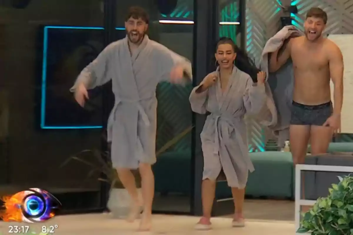 Three smiling people come out of a room, two in gray robes and one in underwear, in a modern and colorful setting. Three smiling people come out of a room, two in gray robes and one in underwear, in a modern and colorful setting.