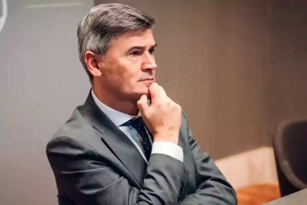 Hombre de cabello canoso con traje gris sentado y pensativo con la mano en el mentón