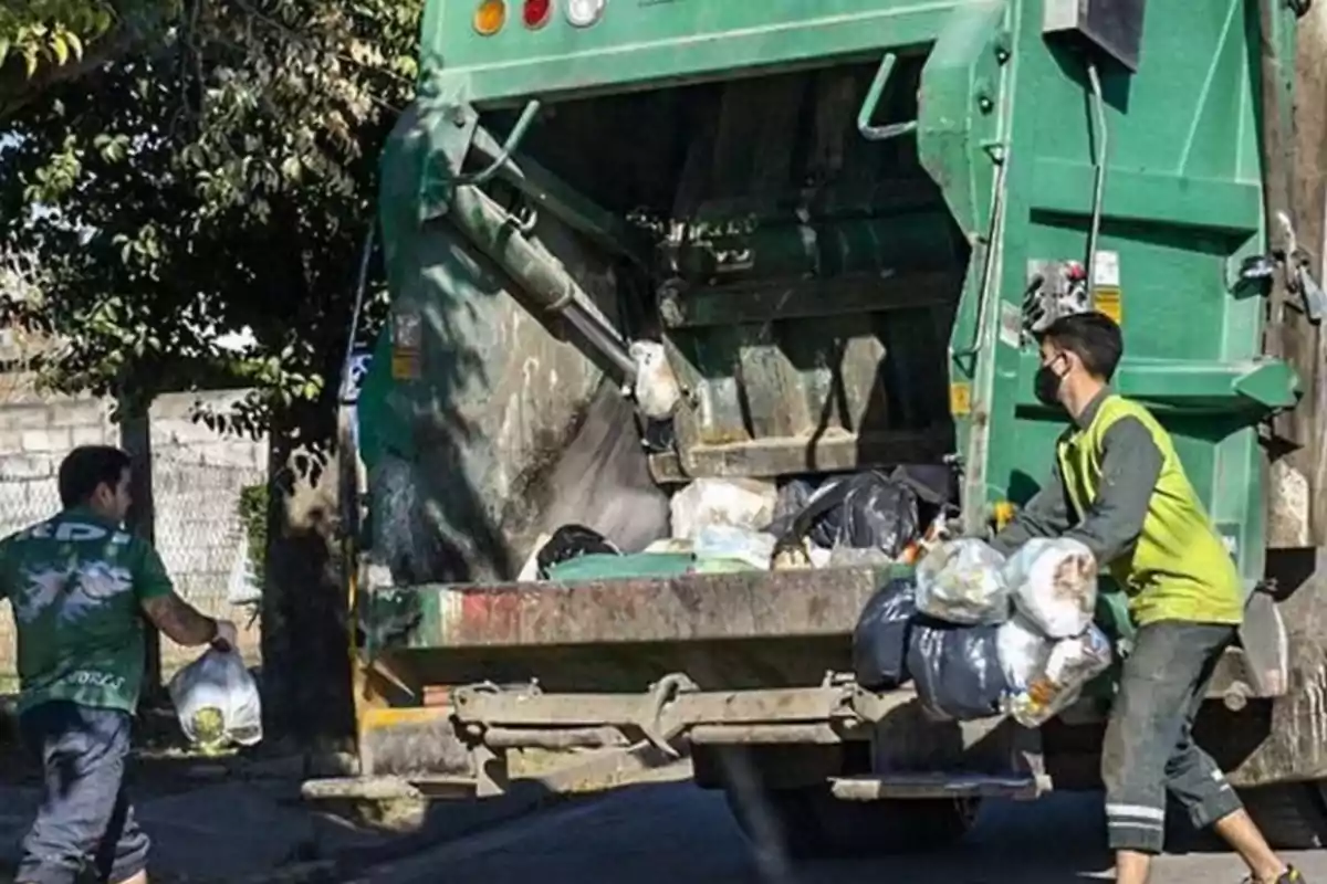 Trabajadores de recolección de basura cargan bolsas y las colocan en la parte trasera de un camión recolector en la calle