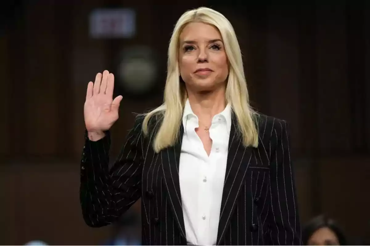 Mujer rubia con traje de rayas levantando la mano derecha en señal de juramento en un entorno formal
