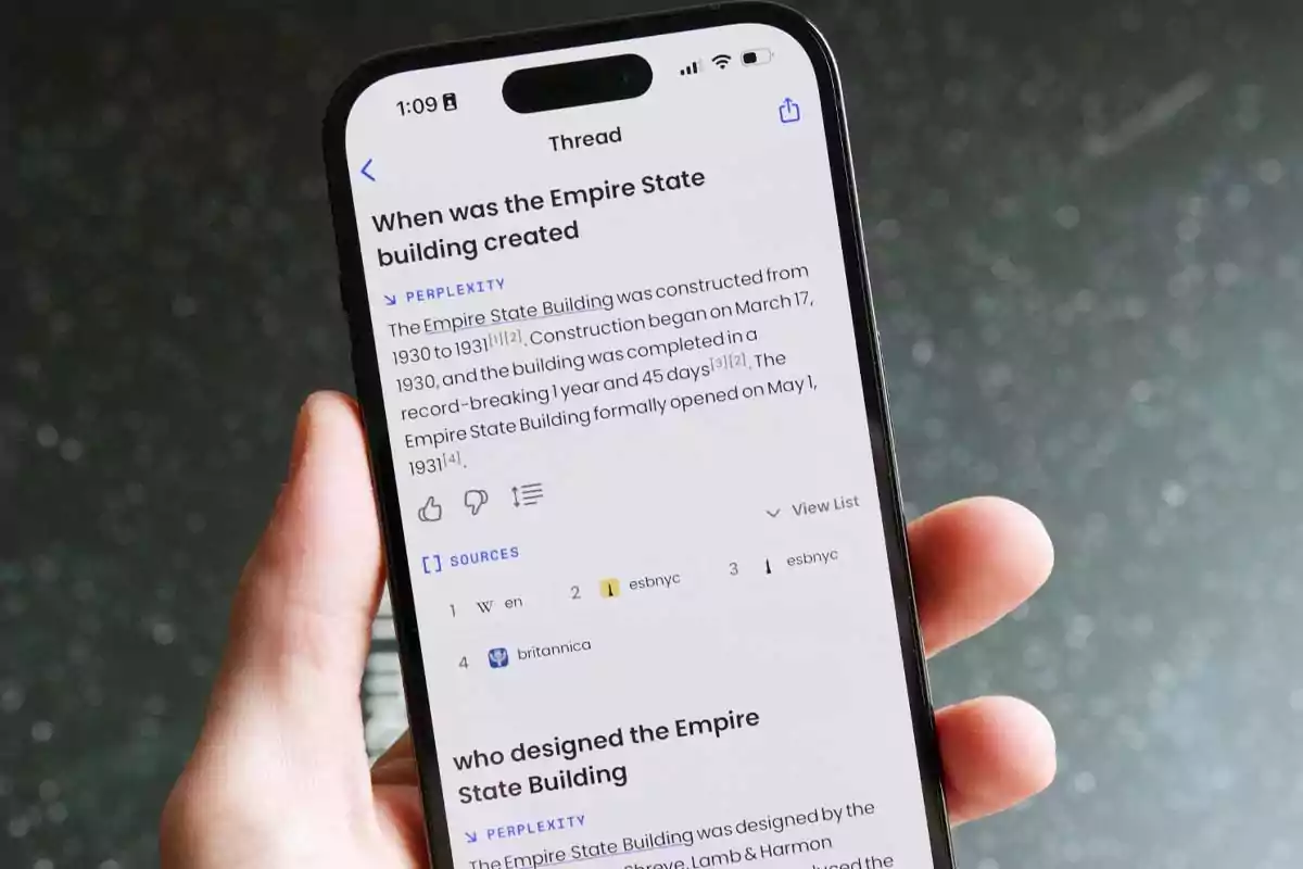 Person holding a smartphone displaying a screen with information about the construction of the Empire State Building Person holding a smartphone displaying a screen with information about the construction of the Empire State Building
