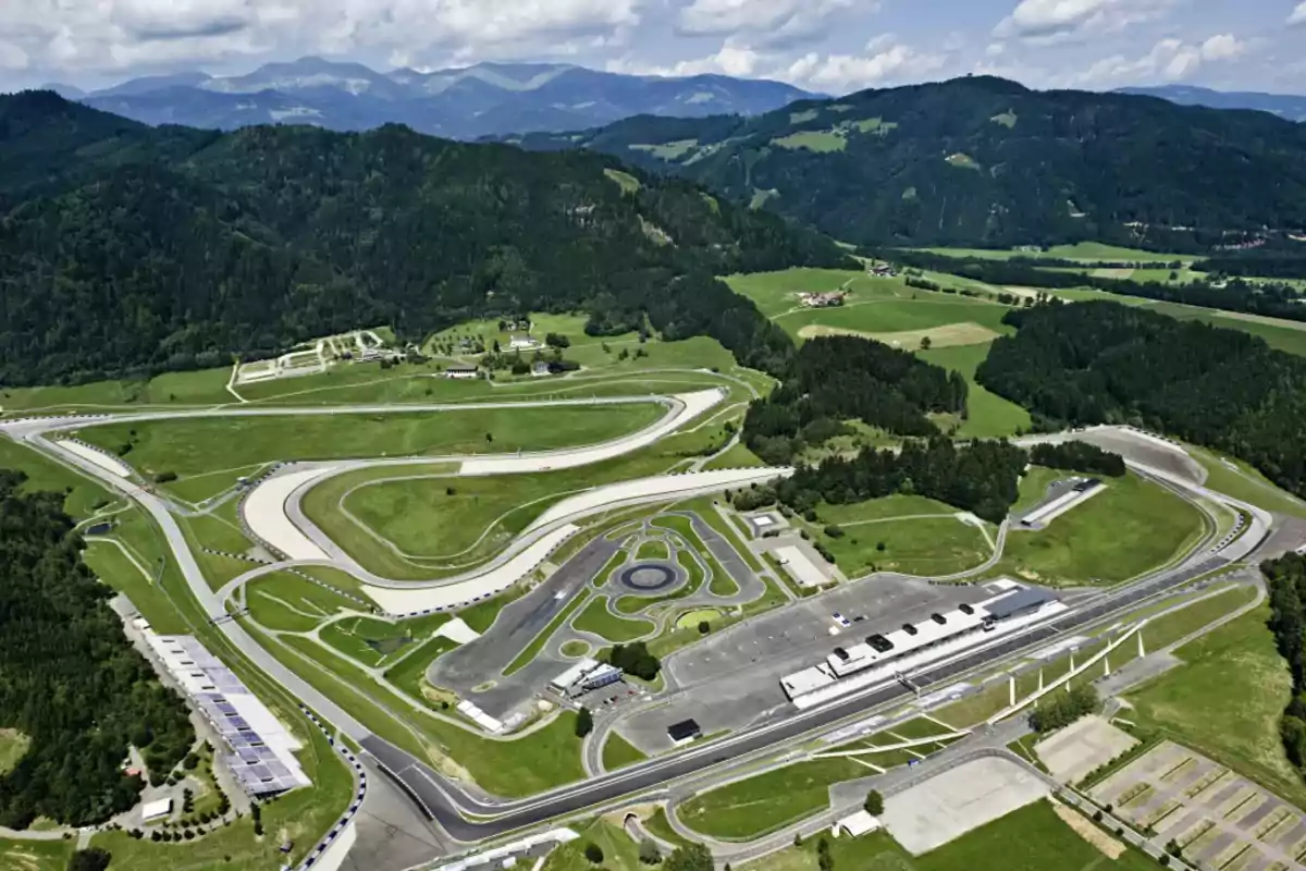 Vista aérea de un circuito de carreras rodeado de montañas y áreas verdes Vista aérea de un circuito de carreras rodeado de montañas y áreas verdes