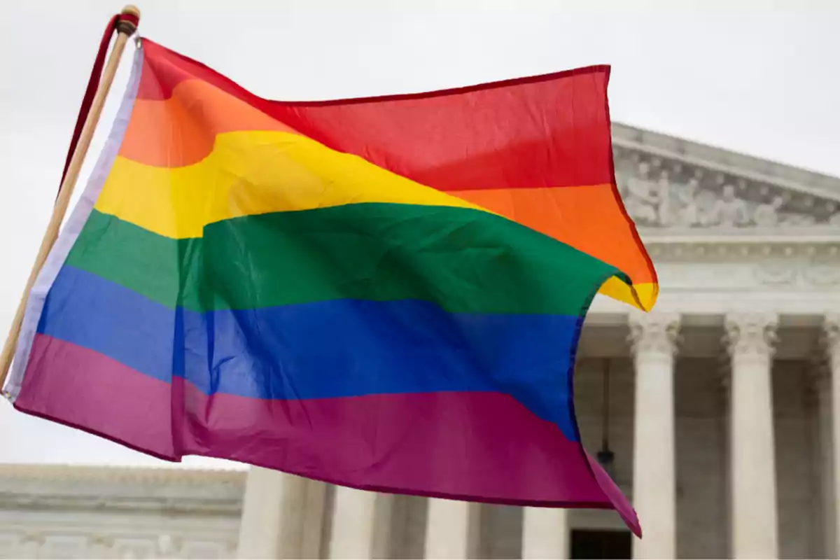Bandera del orgullo LGBT ondeando frente a un edificio gubernamental de columnas blancas