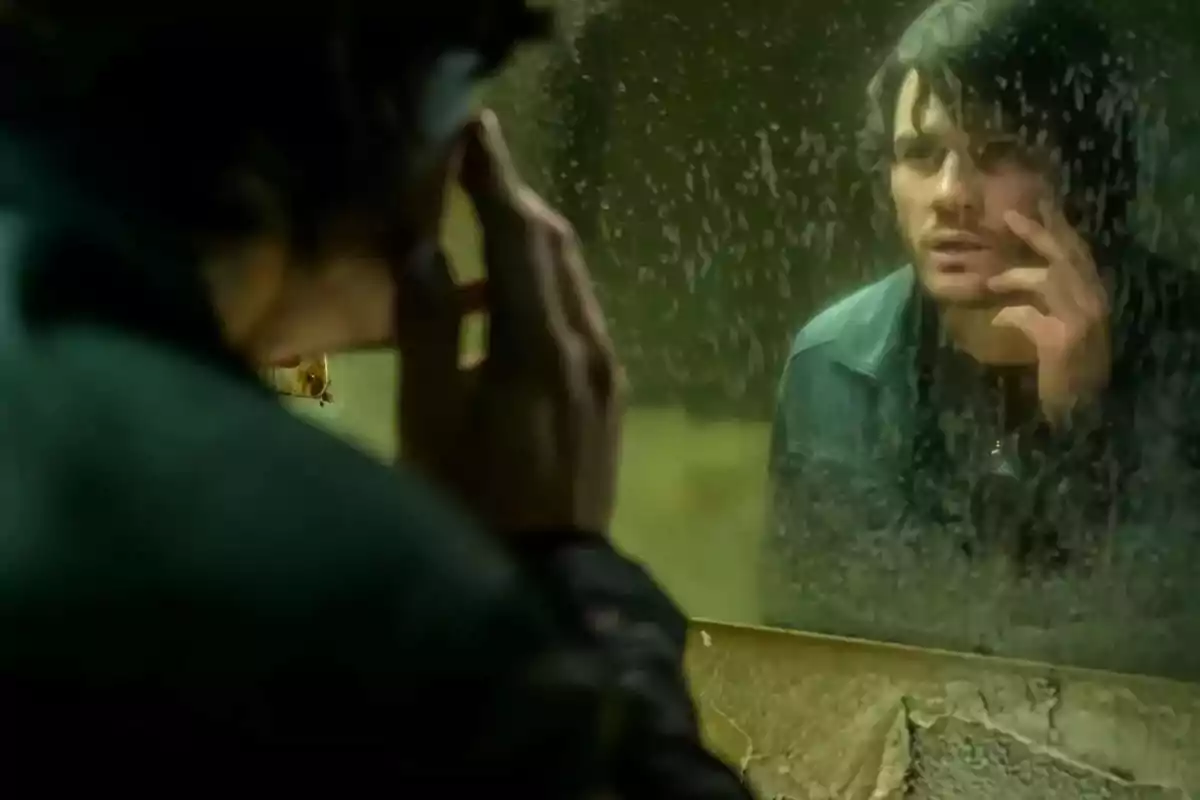Hombre mirando su reflejo en un espejo sucio con expresión pensativa y tocándose la cara Hombre mirando su reflejo en un espejo sucio con expresión pensativa y tocándose la cara