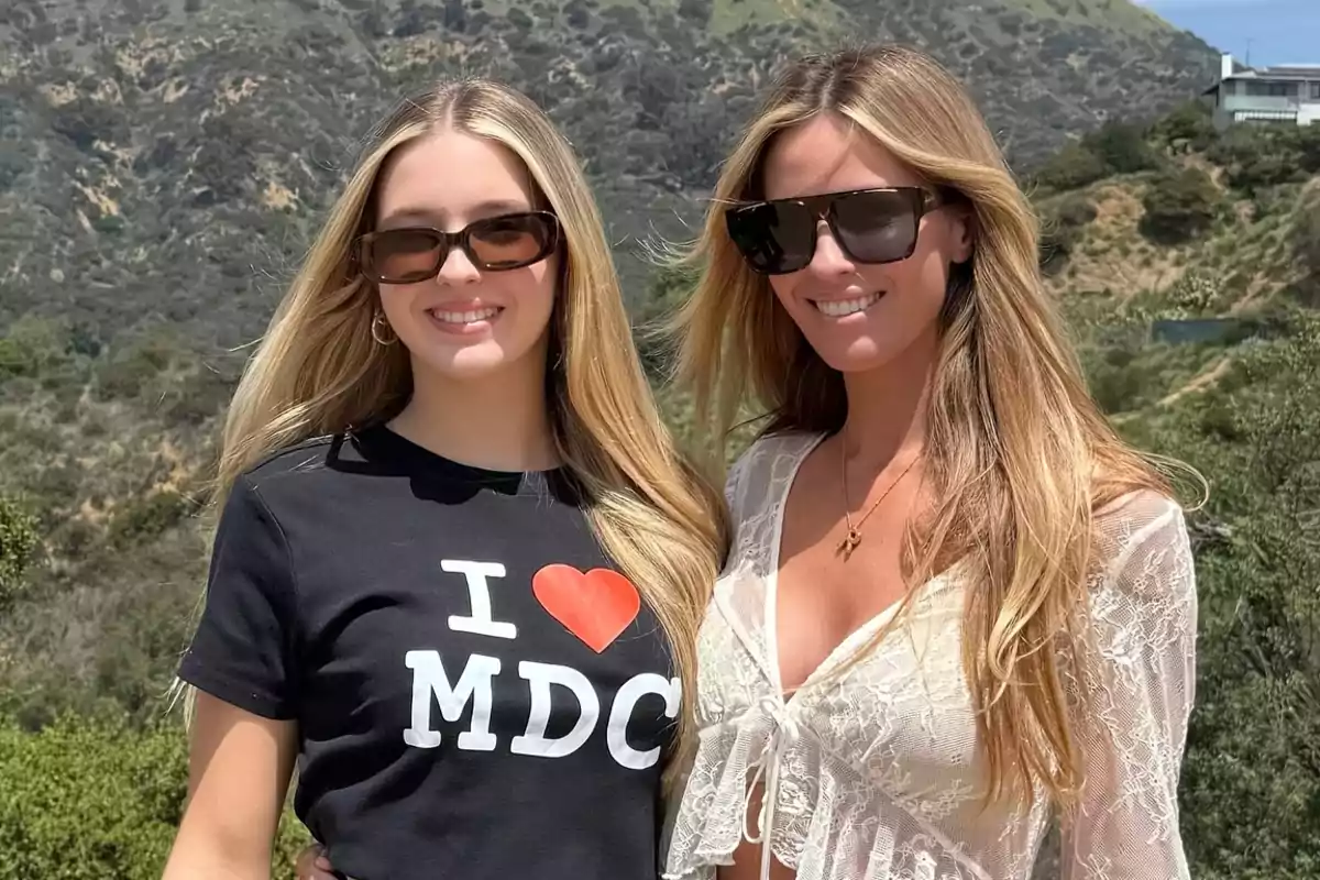Dos mujeres jóvenes con gafas de sol sonríen al aire libre con colinas verdes de fondo