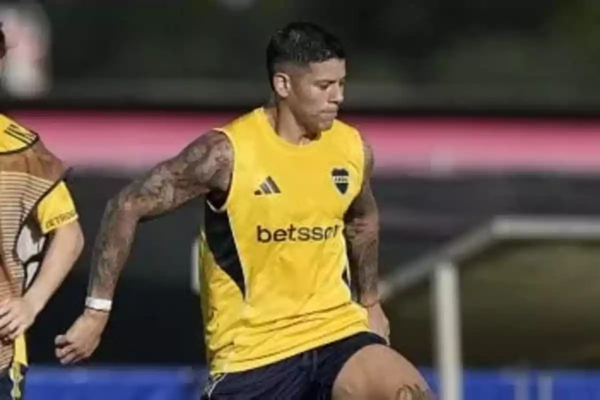 Futbolista con camiseta de entrenamiento amarilla de Boca Juniors corriendo en una cancha durante una práctica