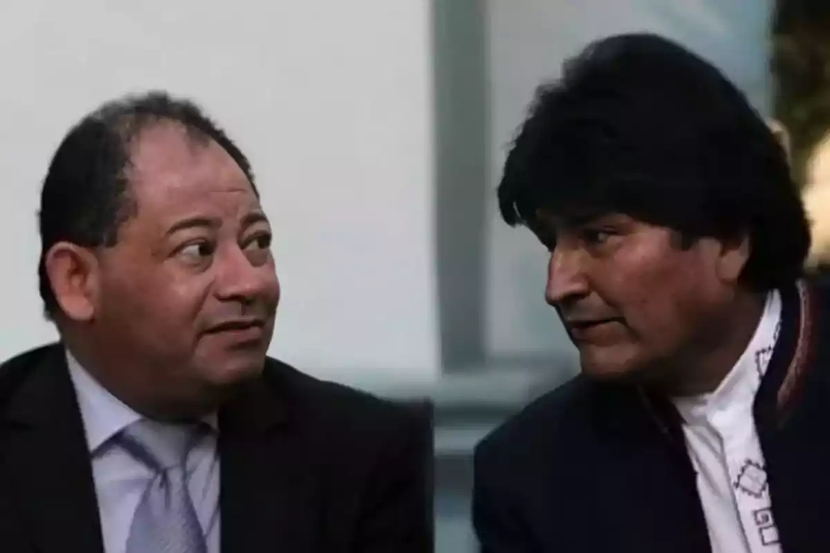 Dos hombres conversan mirándose de frente en un ambiente interior.