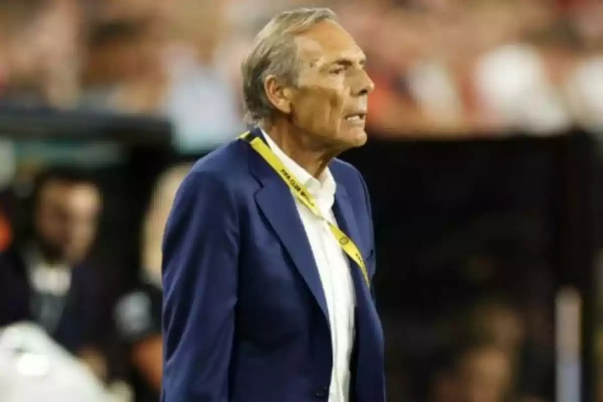 Hombre de cabello canoso con saco azul y camisa blanca de pie en un estadio de fútbol con un gafete amarillo colgado del cuello Hombre de cabello canoso con saco azul y camisa blanca de pie en un estadio de fútbol con un gafete amarillo colgado del cuello