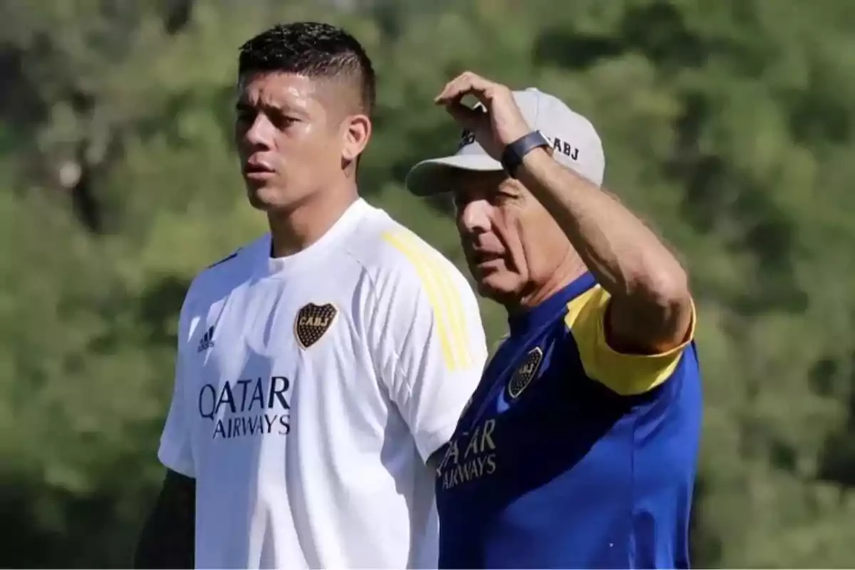Dos personas con ropa de entrenamiento de Boca Juniors observan algo fuera de cámara en un entorno al aire libre. Dos personas con ropa de entrenamiento de Boca Juniors observan algo fuera de cámara en un entorno al aire libre.