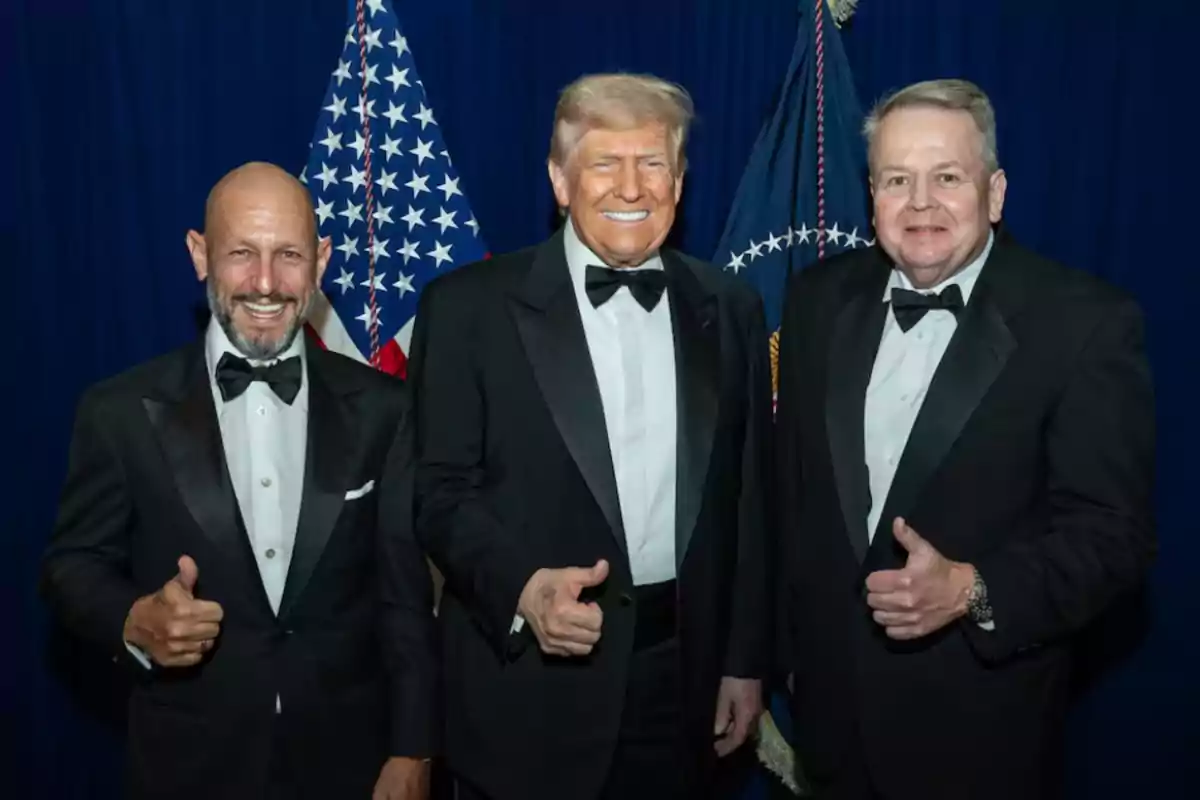 Tres hombres vestidos de esmoquin posan sonriendo y haciendo el gesto de pulgar arriba frente a banderas de Estados Unidos Tres hombres vestidos de esmoquin posan sonriendo y haciendo el gesto de pulgar arriba frente a banderas de Estados Unidos