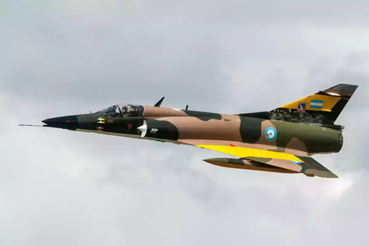Avión de combate con camuflaje volando en el cielo con insignias de la Fuerza Aérea Argentina