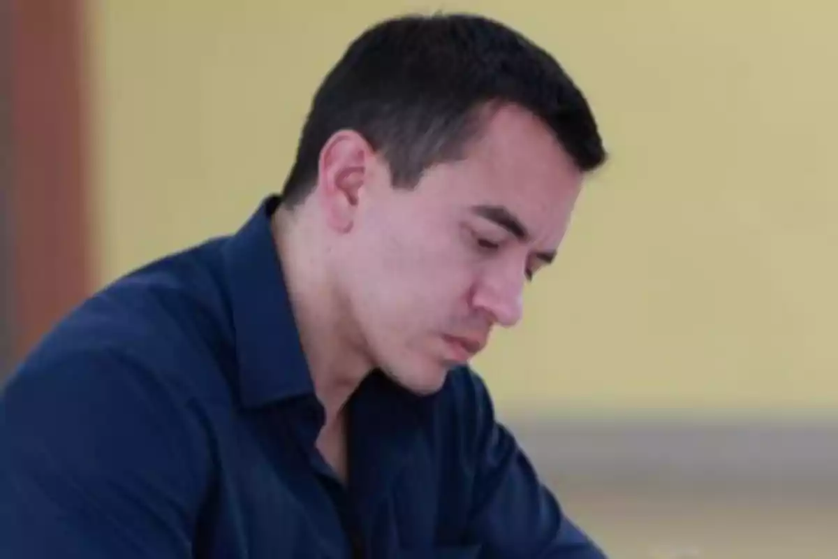 Hombre de cabello corto y oscuro con camisa azul concentrado en escribir o leer algo en una mesa