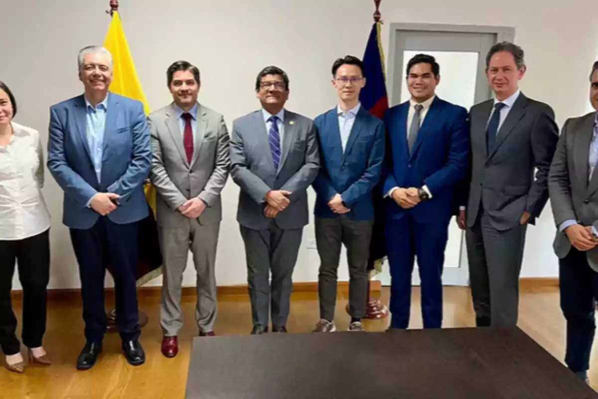 Eight people stand posing in an office, most wearing formal suits, with two flags in the background. Eight people stand posing in an office, most wearing formal suits, with two flags in the background.