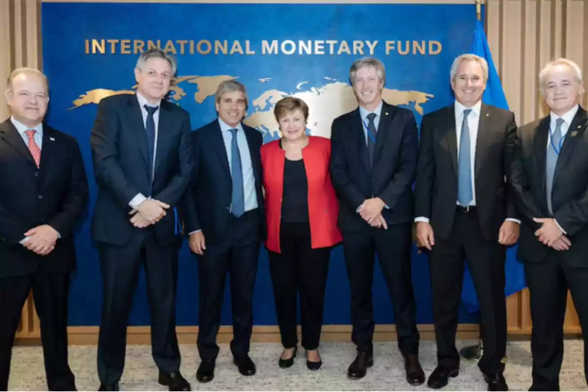 Grupo de personas vestidas de traje posando frente a un cartel azul con letras doradas que dice International Monetary Fund