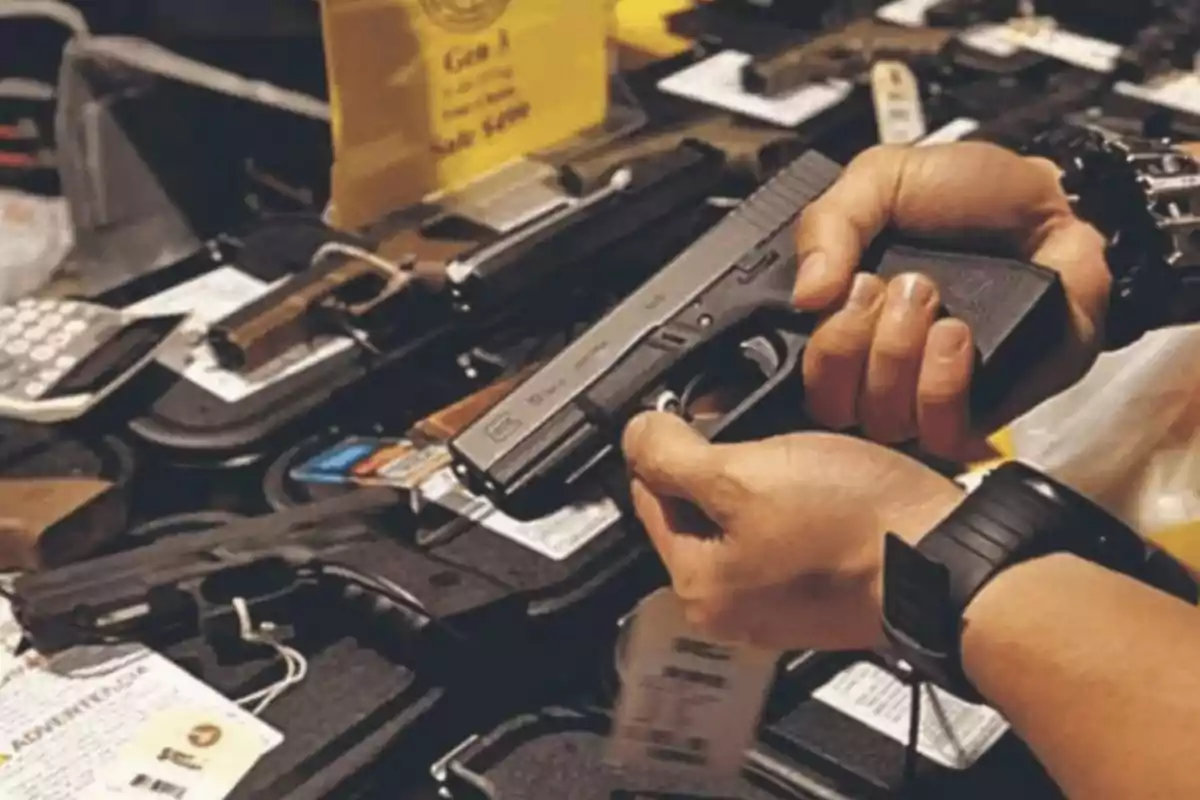Person holding a gun in a gun store with several guns displayed on a table