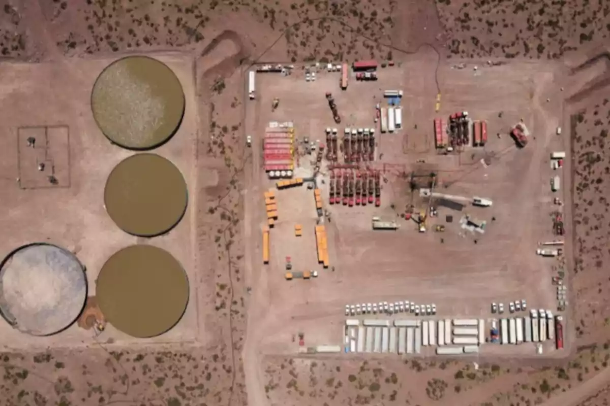 Aerial view of an industrial plant in the desert with several circular tanks and numerous vehicles and equipment distributed across the site. Aerial view of an industrial plant in the desert with several circular tanks and numerous vehicles and equipment distributed across the site.