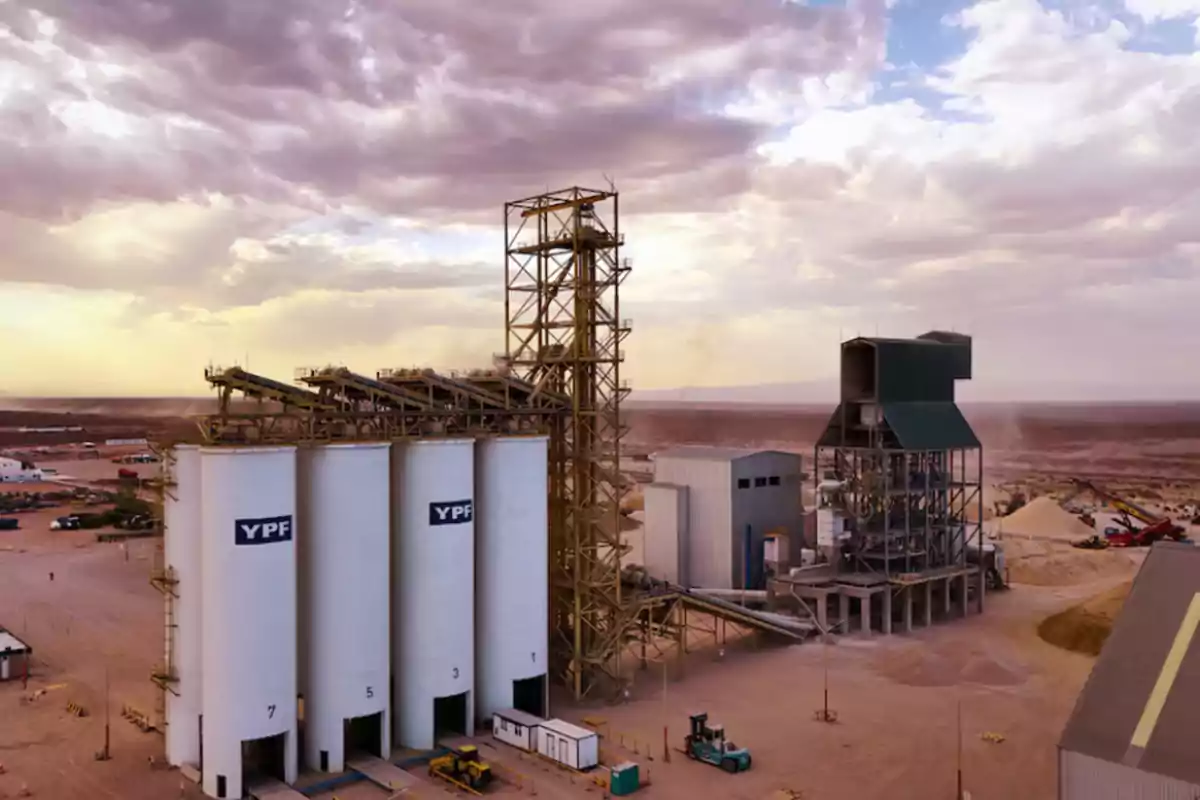 View of a YPF industrial plant in the middle of the desert with white silos and metal structures under a cloudy sky at sunset