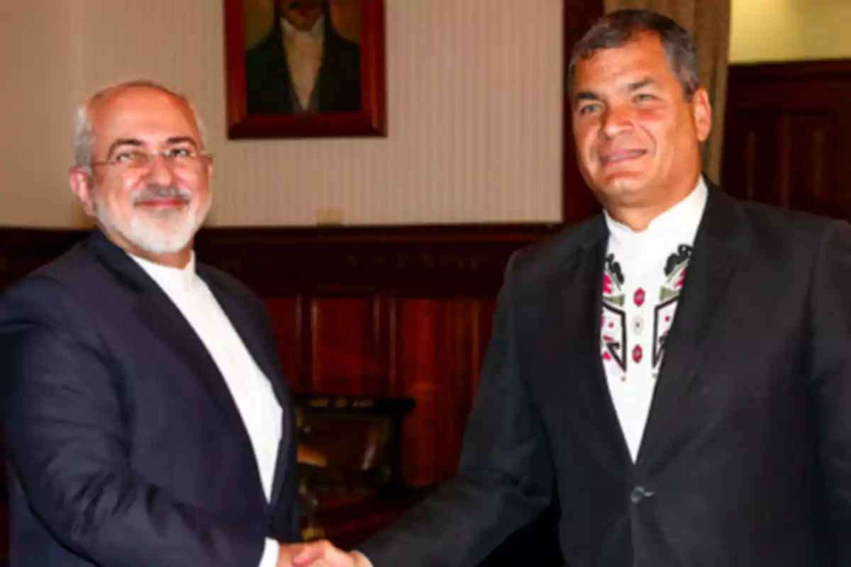 Two men in suits shake hands in an elegant room with wooden walls and a portrait in the background.