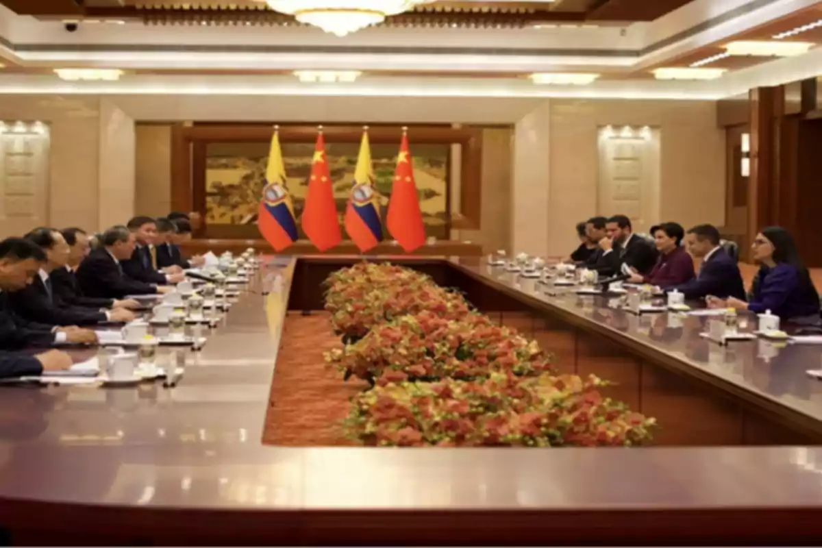 Diplomatic meeting between delegations from Ecuador and China in a conference room with both countries’ flags in the background and a long table decorated with flowers. Diplomatic meeting between delegations from Ecuador and China in a conference room with both countries’ flags in the background and a long table decorated with flowers.