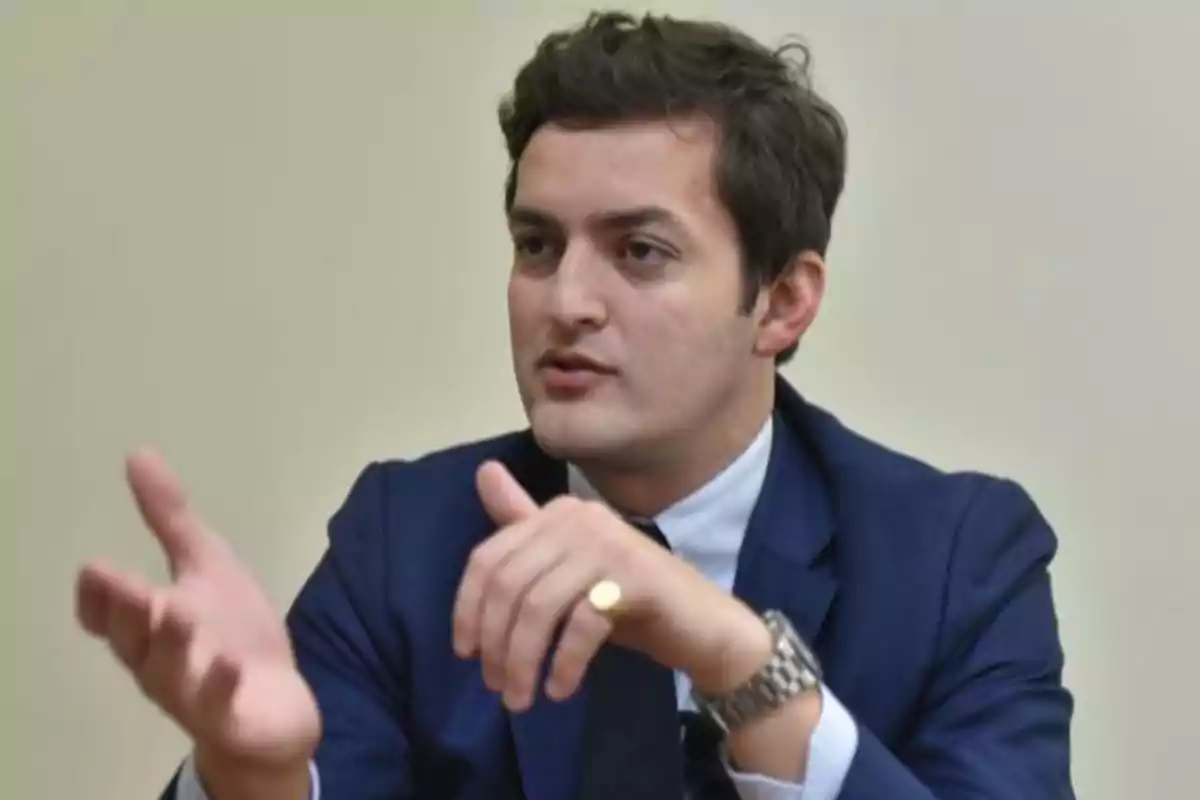 Young man in a blue suit gesturing while speaking in an indoor setting