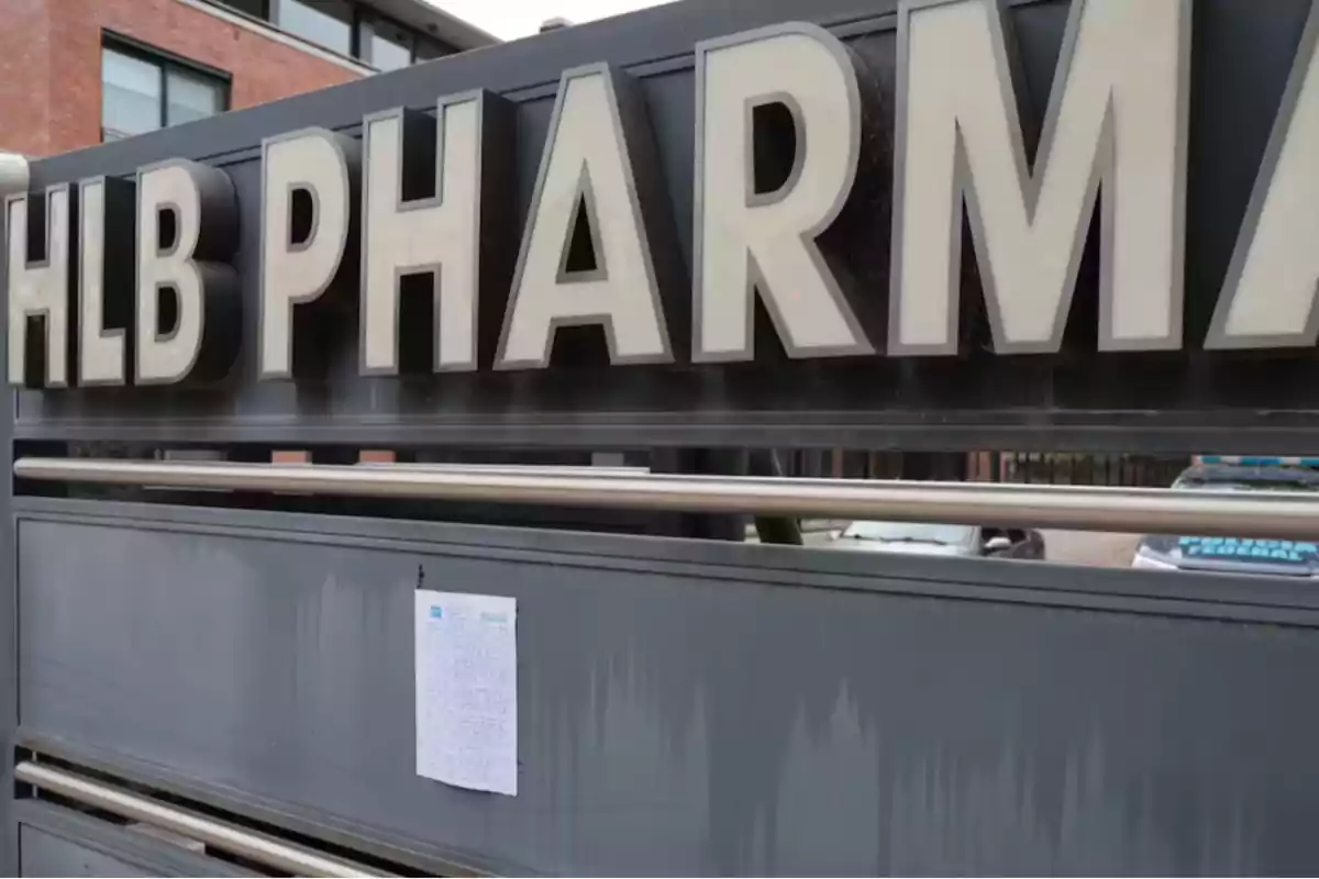 Letrero grande de una farmacia con letras blancas y un papel con texto pegado en la parte inferior del letrero