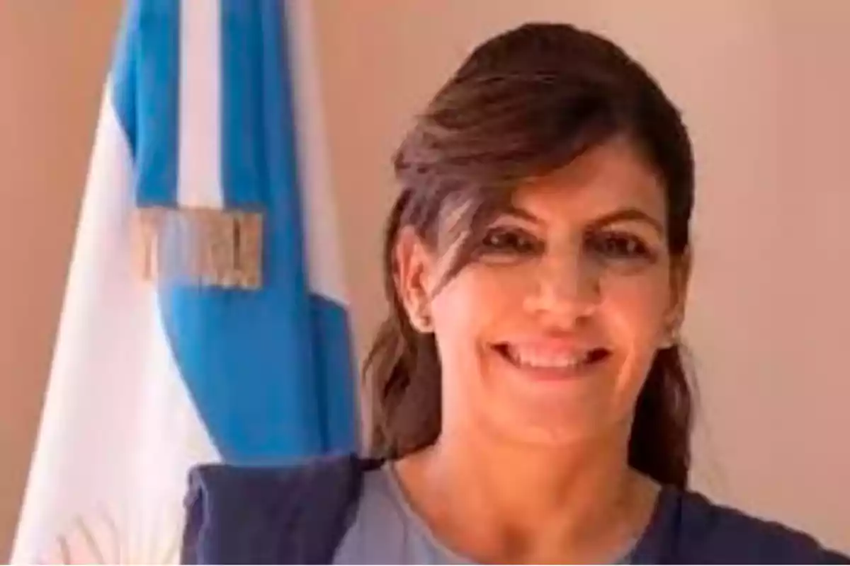 Mujer sonriente de cabello castaño con una bandera argentina de fondo