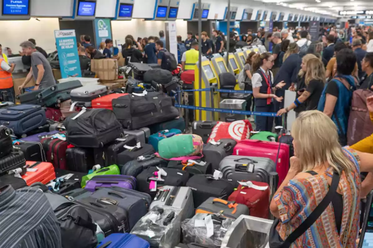Large number of suitcases stacked at an airport with many people lining up in the check-in area Large number of suitcases stacked at an airport with many people lining up in the check-in area