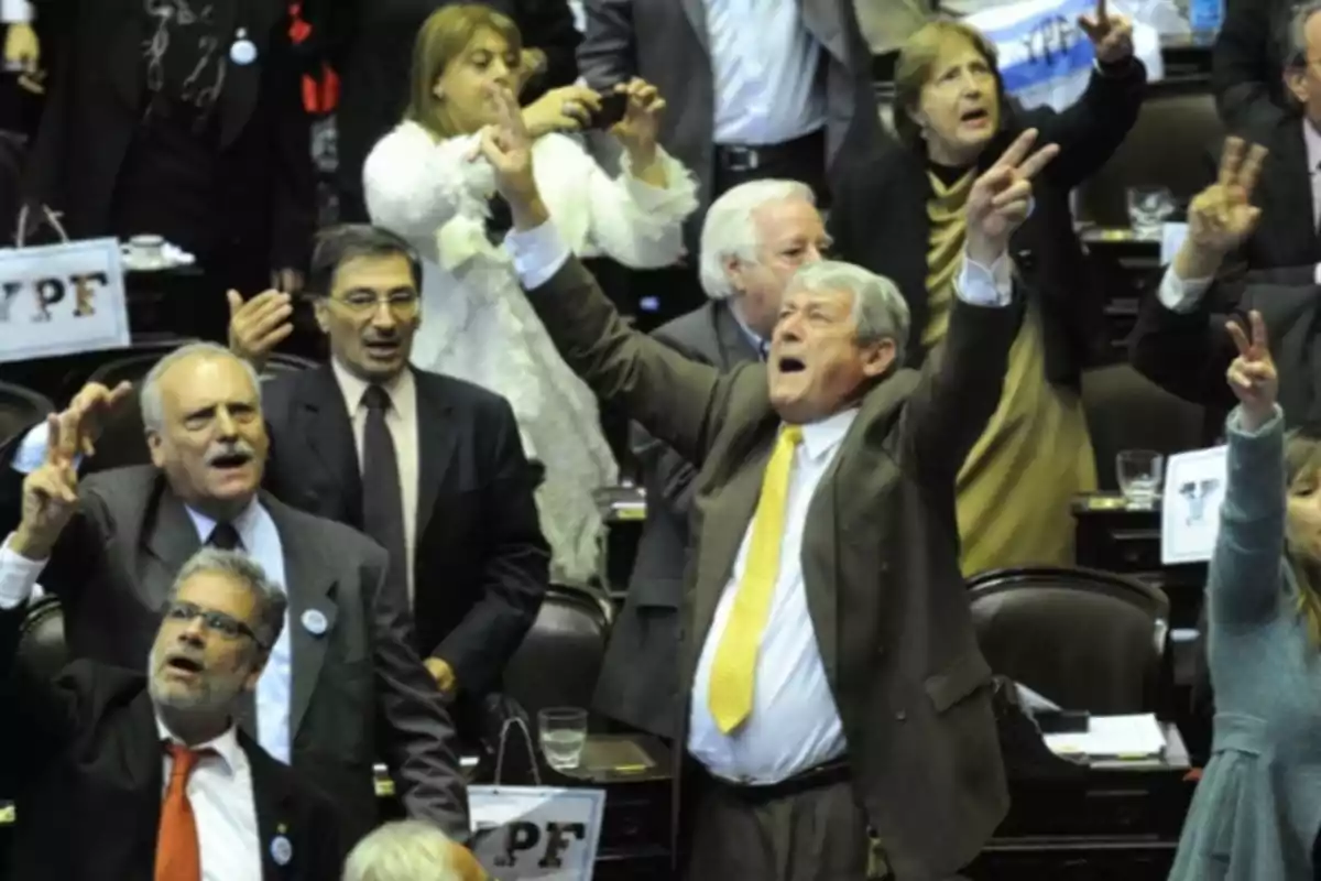 A group of people in a parliamentary chamber celebrating with their arms raised and making the victory sign with their fingers A group of people in a parliamentary chamber celebrating with their arms raised and making the victory sign with their fingers