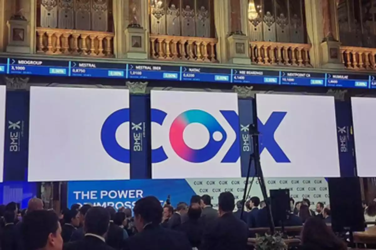 Personas reunidas en un evento financiero con pantallas grandes que muestran el logo de COX en un edificio elegante